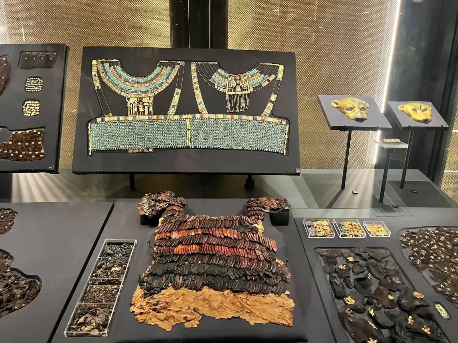 Collares anchos de cuentas turquesa, cabezas de felino doradas y restos de prendas de cuero del ajuar de Tutankamón en una vitrina