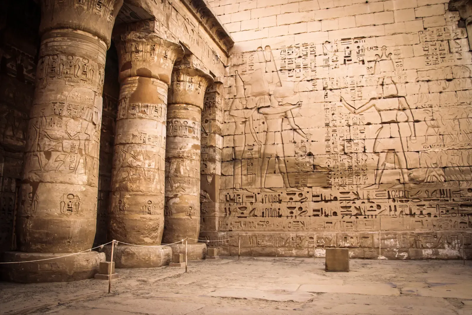 Temple courtyard with massive columns and a wall carved with large figures and columns of hieroglyphs in sunk relief
