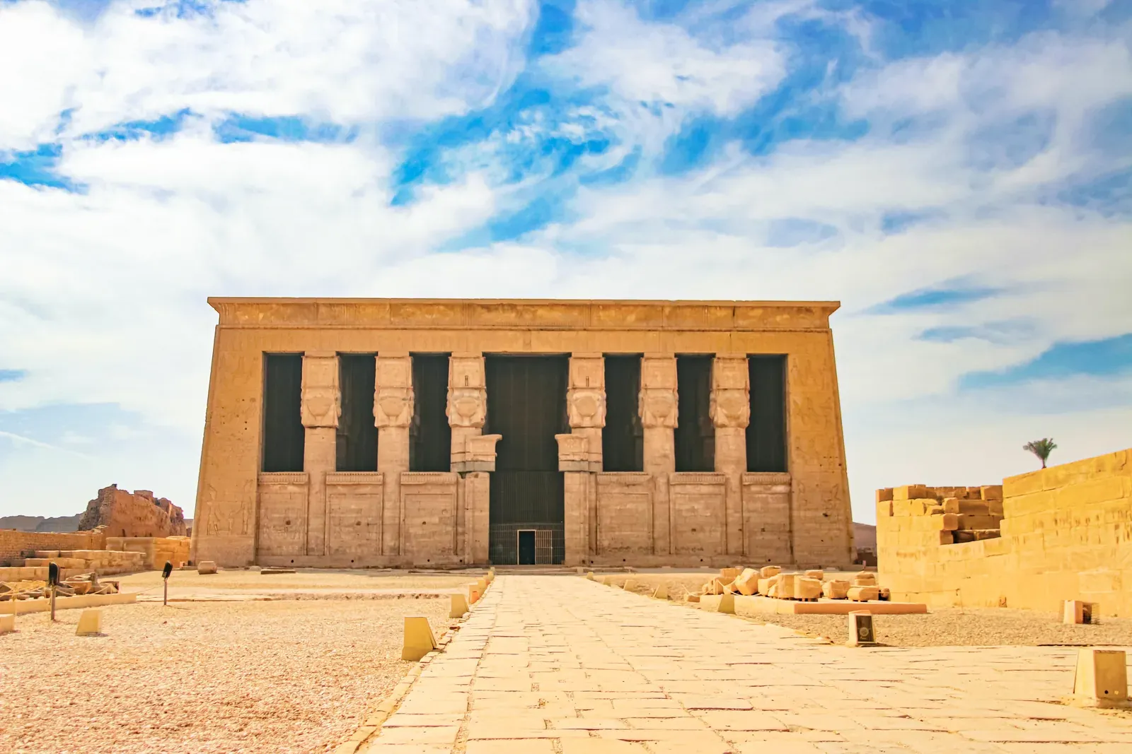 Fachada del templo de Hathor en Dendera, con columnas rematadas por la cabeza de Hathor bajo un cielo azul