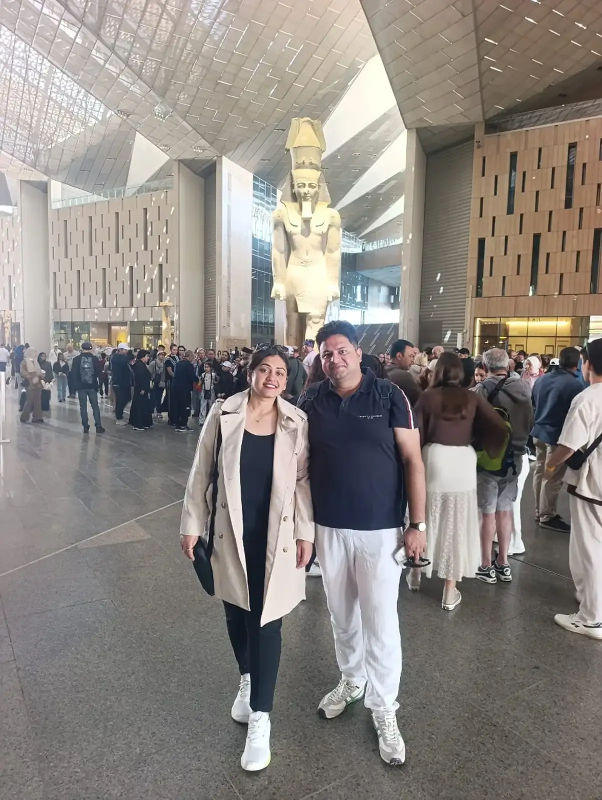 Dos viajeros de Nile Empire posan ante el coloso de Ramsés II en el Gran Atrio del Gran Museo Egipcio, rodeados de otros visitantes