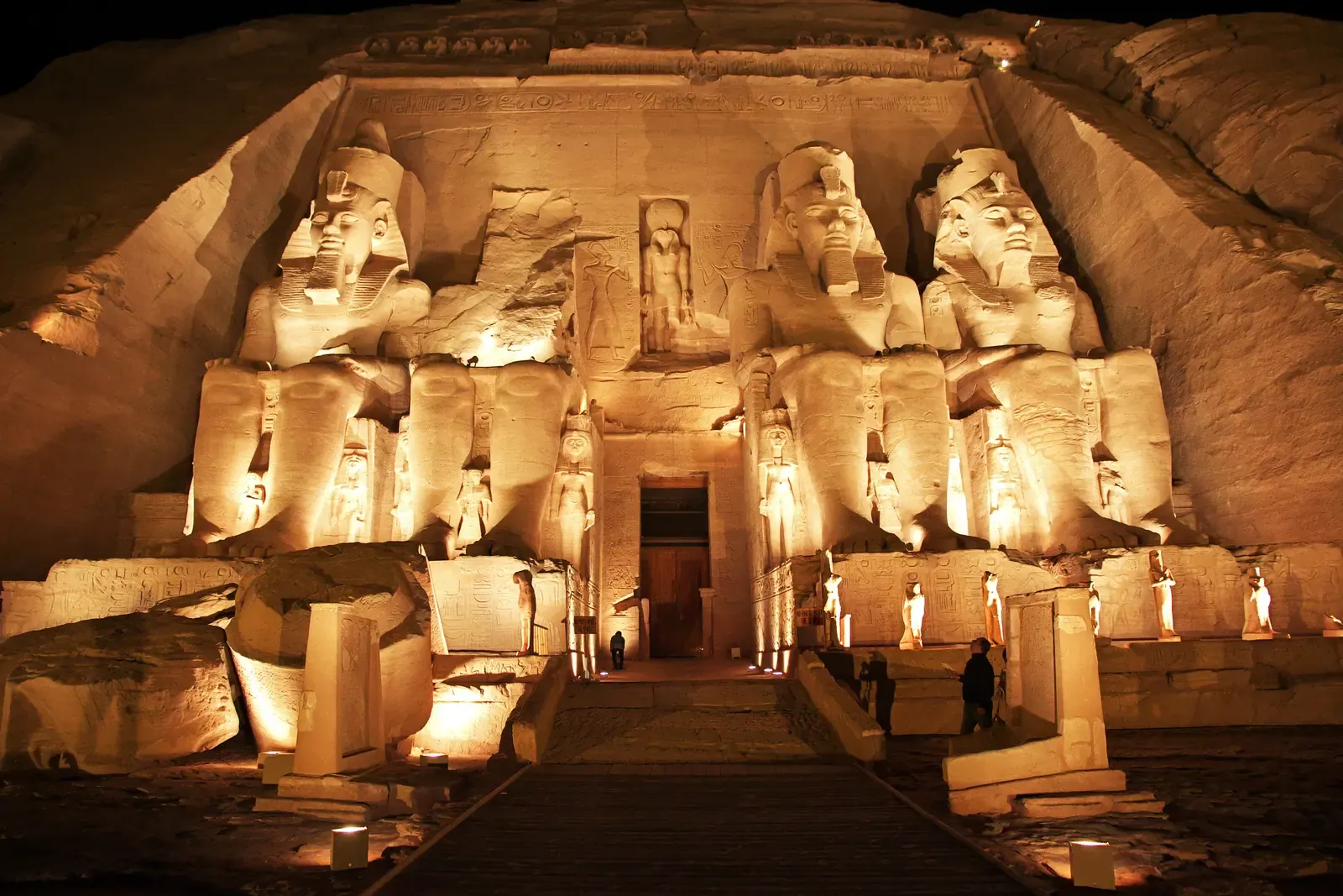 Fachada excavada en la roca del Gran Templo de Abu Simbel iluminada de noche, con estatuas colosales sedentes a ambos lados de la entrada