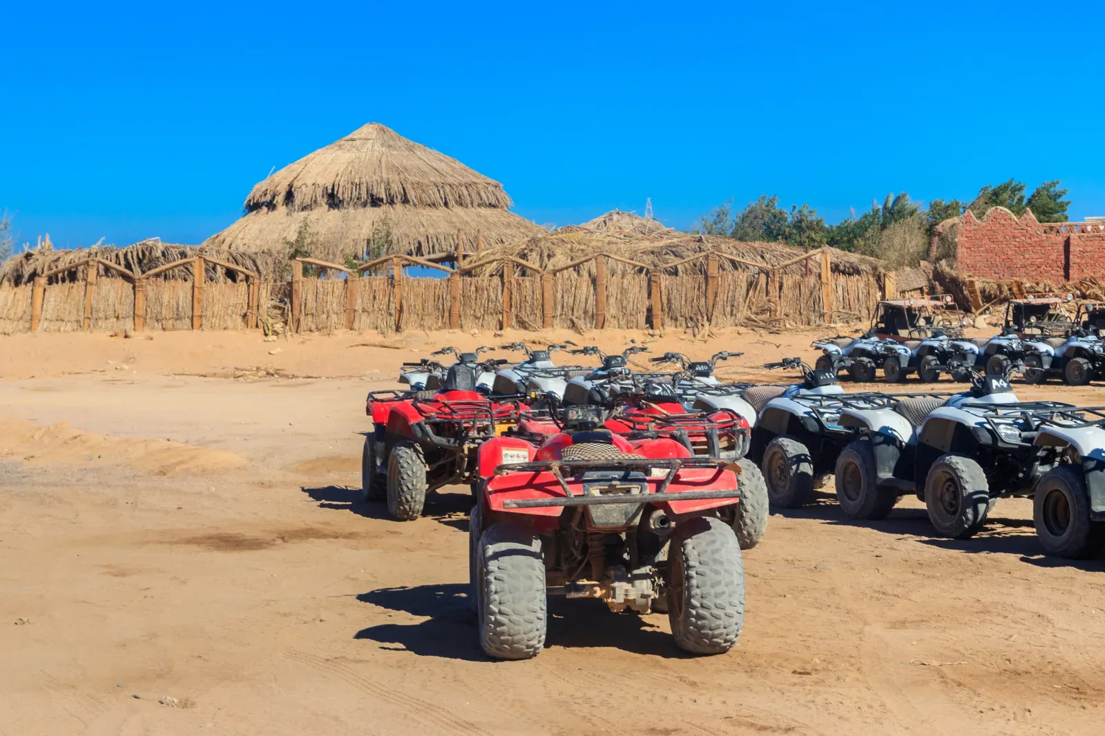 Quad bikes lined up at a desert camp with thatched shelters