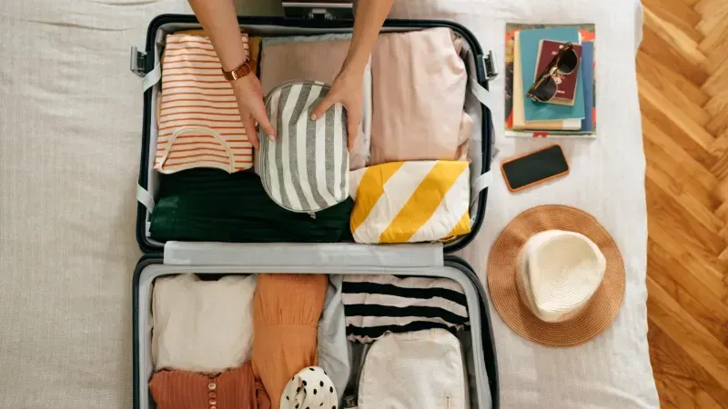 Maleta abierta con ropa ligera, sombrero y gafas de sol, preparada para un viaje a Egipto