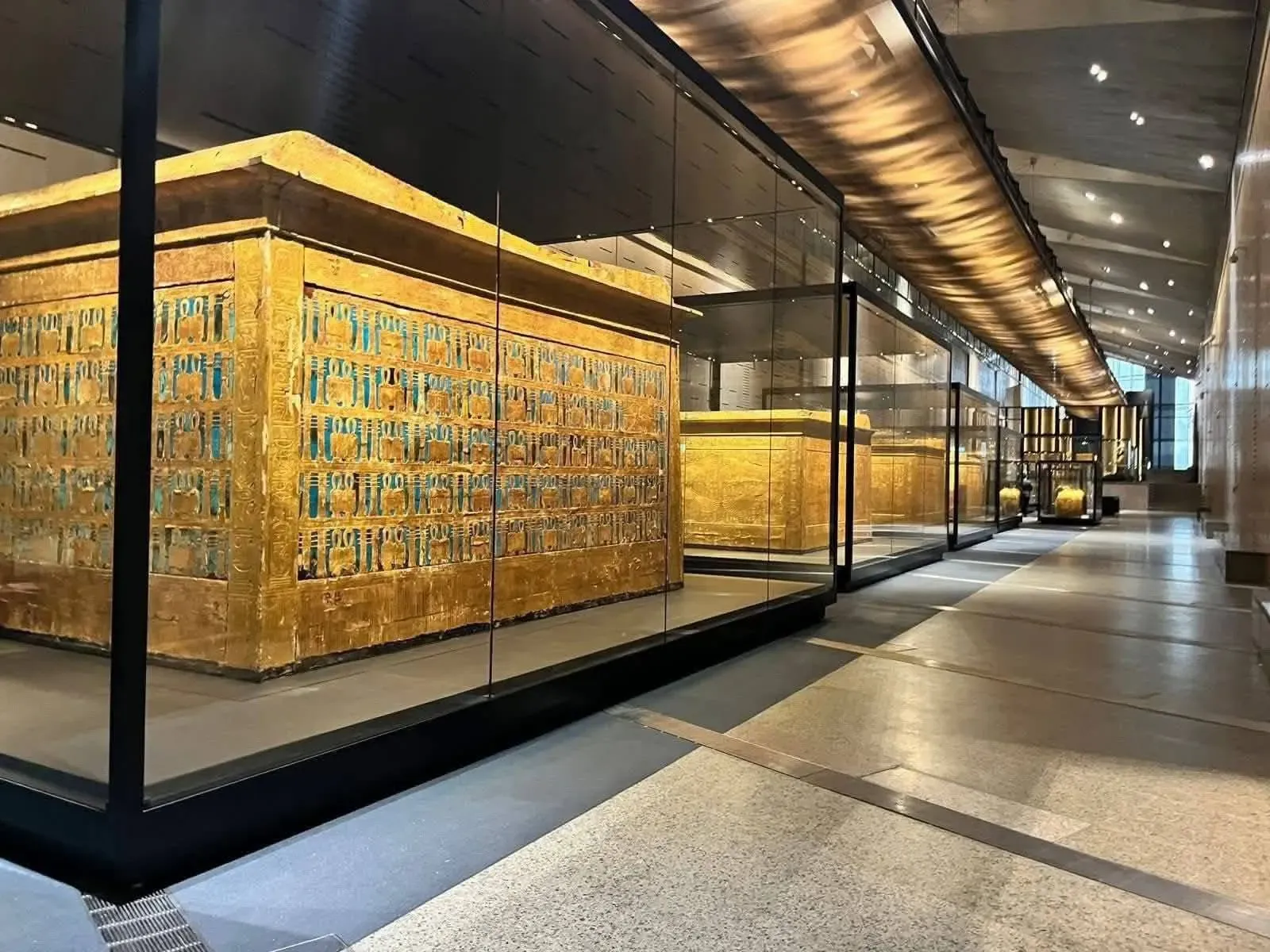 Capillas doradas de Tutankamón expuestas en fila dentro de vitrinas en una galería del Gran Museo Egipcio