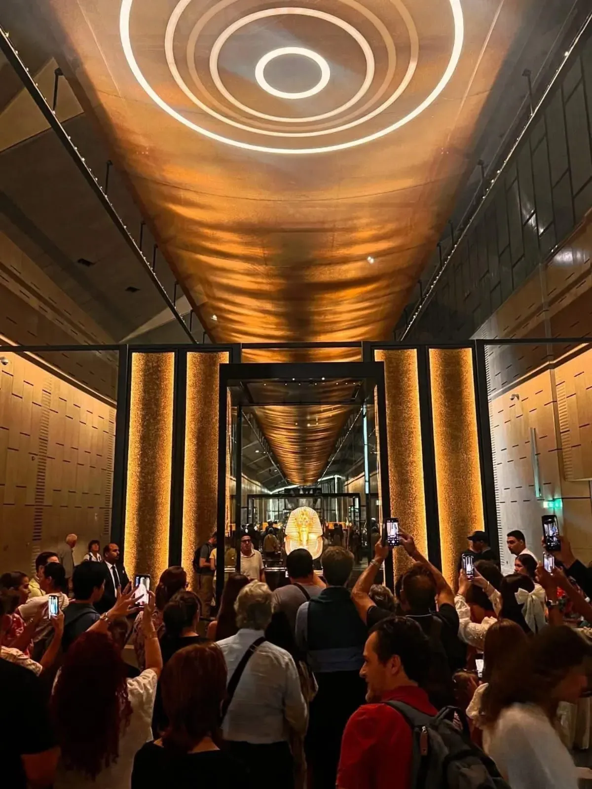 Visitantes fotografían con el móvil la máscara de oro de Tutankamón al fondo de la sala en el Gran Museo Egipcio